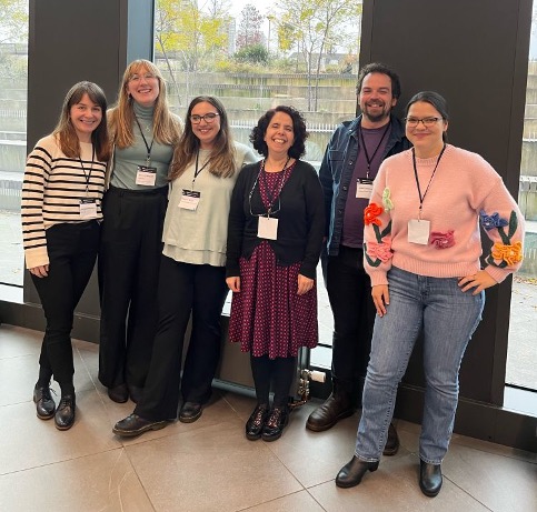 Six members of the Salgado lab standing together indoors in front of tall windows, wearing conference badges and smiling.